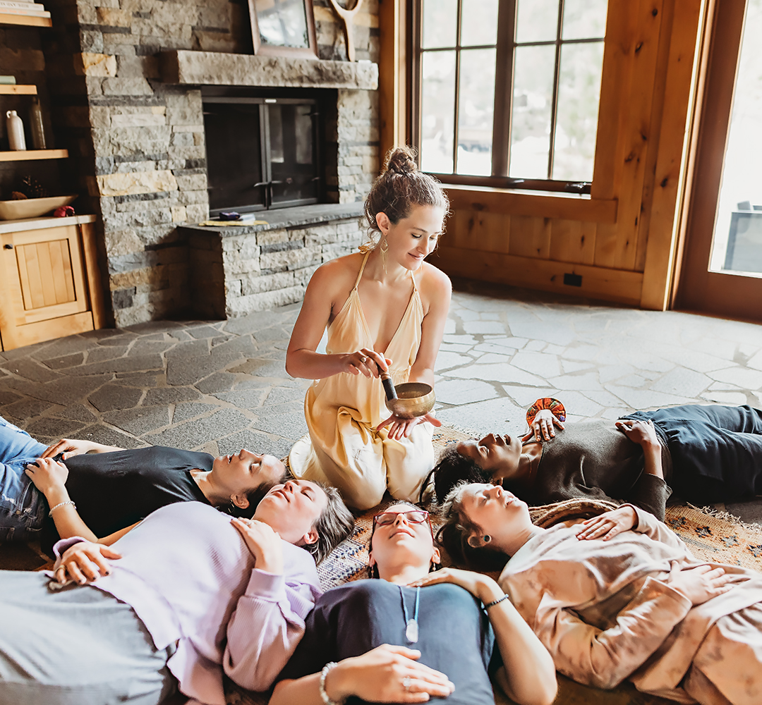 Adrienne Rivera holding a singing bowl over a circle of participants lying down during a breathwork journey